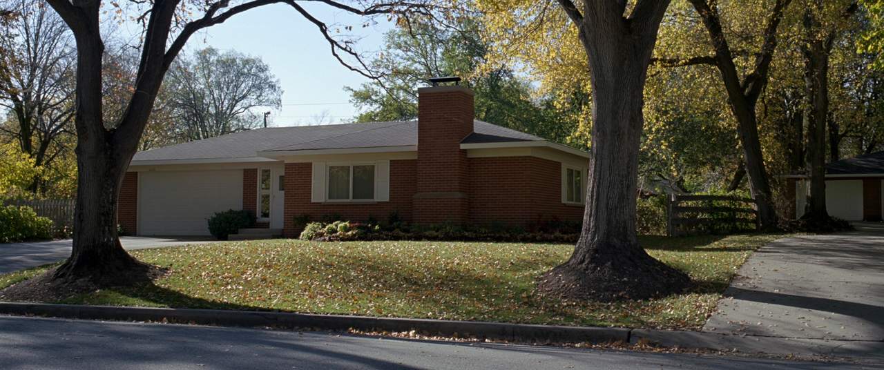 Mid-century brick ranch home with a masonry chimney on a tree-lined Michigan street in autumn