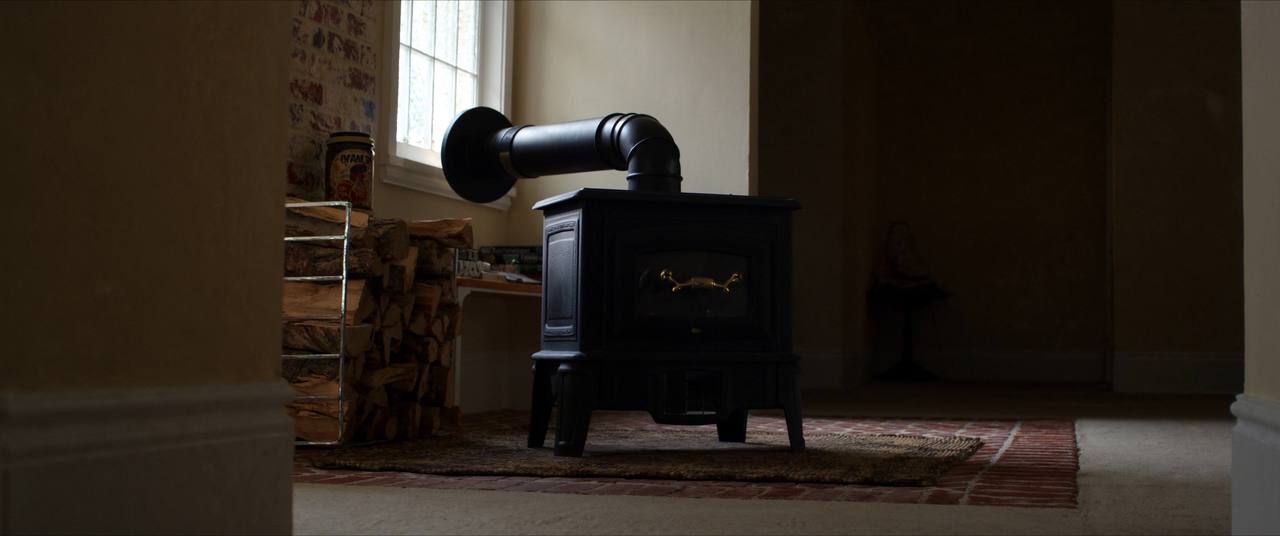 Cast iron wood stove on a brick hearth with split firewood stacked beside it