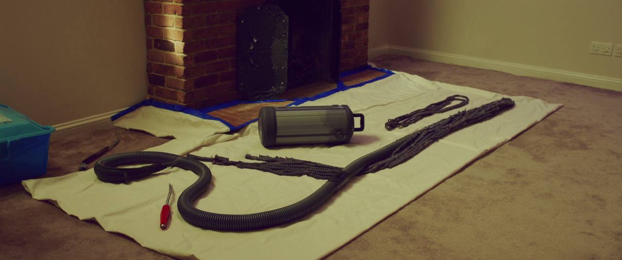 Chimney sweeping rods and a rotary brush head laid out on a drop cloth beside a fireplace hearth